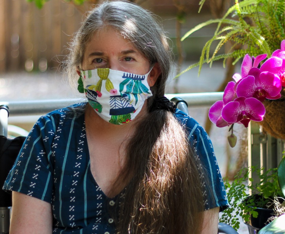 Ingrid wearing a colorful cloth face-mask, sitting next to a fuschia orchid